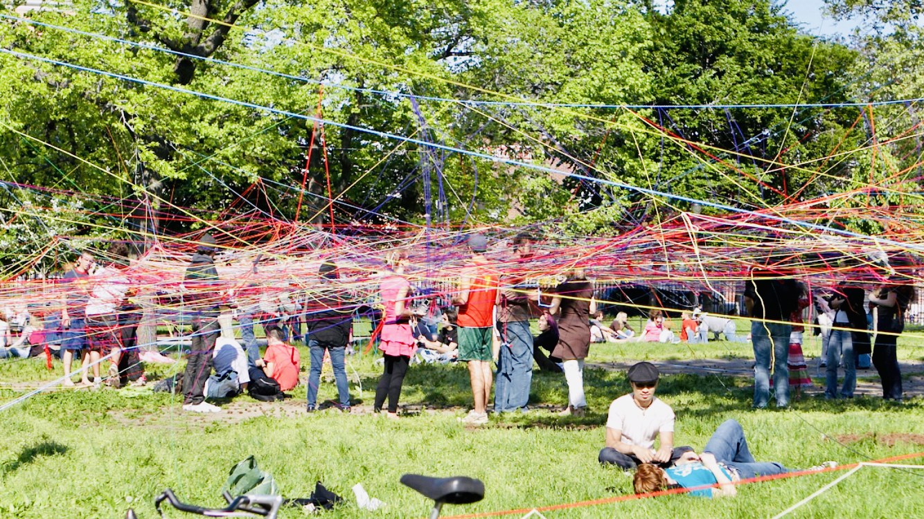 A community gathering weaving colorful strings between trees